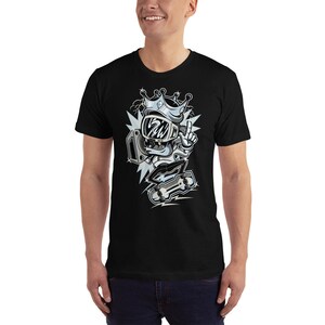 Puede incluir: Camiseta negra con una ilustraci&oacute;n de dibujos animados de un personaje que lleva una corona y sostiene un mando de videojuego. El personaje lleva un casco y gafas protectoras. La ilustraci&oacute;n est&aacute; en tonos grises y blancos.