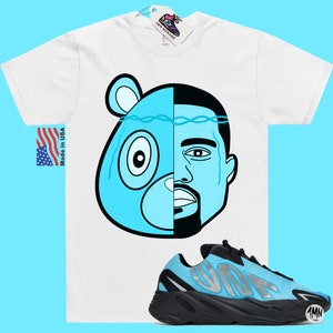 May include: White t-shirt with a blue and black cartoon image of a bear and a man's face. The t-shirt is paired with blue and black sneakers with the word "Yeezy" on the side.