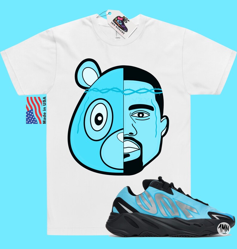 May include: White t-shirt with a blue and black cartoon image of a bear and a man's face. The t-shirt is paired with blue and black sneakers with the word "Yeezy" on the side.