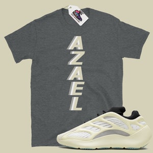 May include: A grey t-shirt with the word "AZAEL" printed vertically in a light beige color. A pair of white and black sneakers with a unique design.