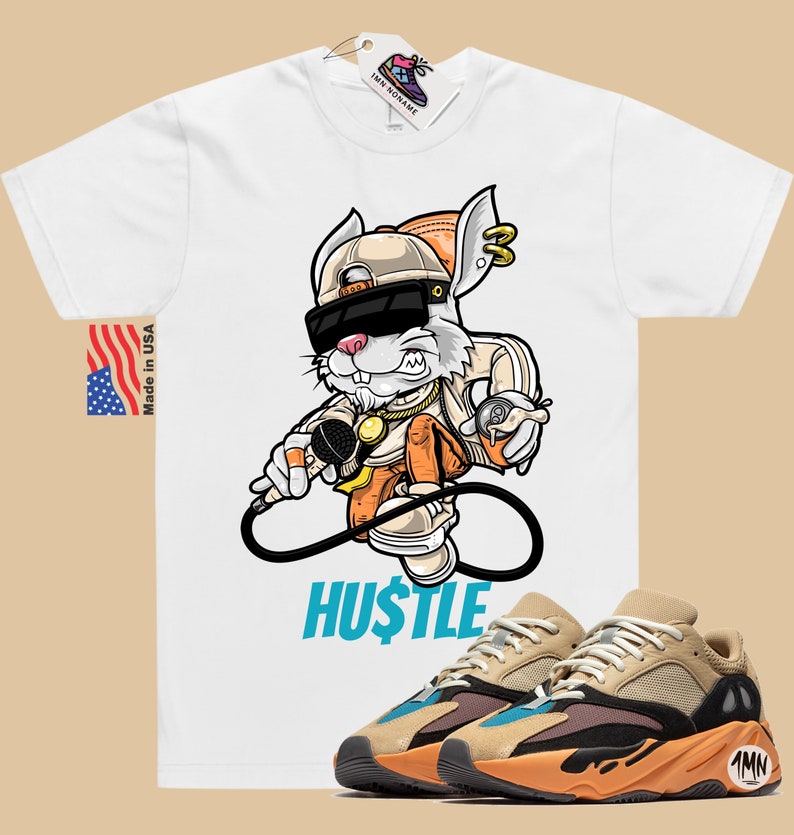 May include: White t-shirt with a cartoon rabbit wearing sunglasses and a gold chain, holding a microphone and a spray can. The text "HUSTLE" is printed below the rabbit. A pair of tan, orange, and blue sneakers are shown below the t-shirt.