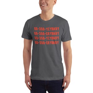 Peut inclure: Un t-shirt gris fonc&eacute; avec le texte "00-350-YZBABY 00-350-CRYBABY 00-350-YZBABY 00-350-CRYBABY" imprim&eacute; en rouge.