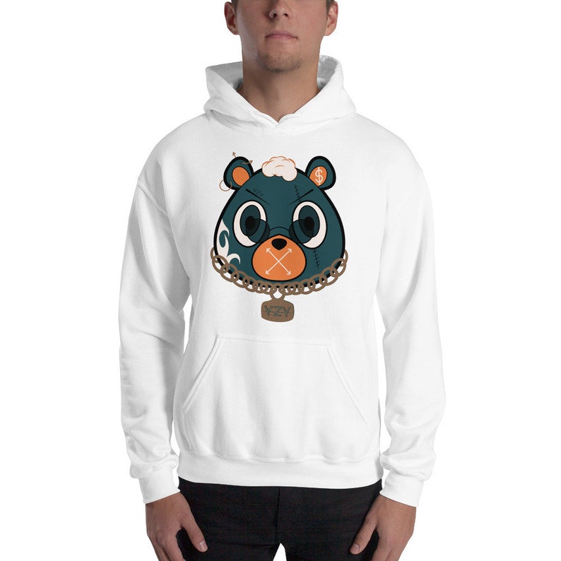 May include: White hooded sweatshirt featuring a cartoon bear face with teal fur, orange cross-stitched mouth, and gold chain necklace. The bear has round glasses and a dollar sign on one ear. The word "NZY" is on a pendant.