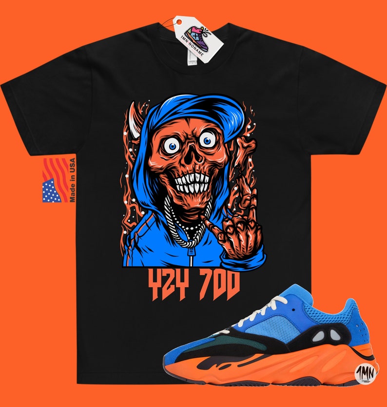 May include: Black t-shirt with a graphic of a skull wearing a blue hoodie and a gold chain. The text "424 700" is printed below the graphic. A pair of blue and orange sneakers are shown below the t-shirt.