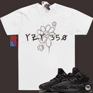 Pode incluir: Camiseta branca com um gr&aacute;fico preto e branco de uma flor e o texto "YZY 350". Abaixo da camiseta, &eacute; mostrado um par de t&ecirc;nis preto e marrom com padr&atilde;o de camuflagem.