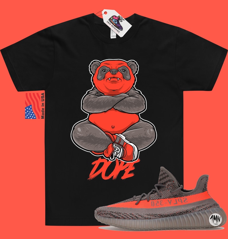 Może przedstawiać: Czarny T-shirt z grafiką czerwonego pandy i nadrukiem słowa "DOPE" poniżej. Panda siedzi ze skrzyżowanymi ramionami i nosi czerwono-białe buty. Na zdjęciu widoczne są r&oacute;wnież buty Yeezy w kolorze szarym i pomarańczowym.