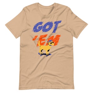 May include: A tan t-shirt with the words "GOT 'EM" in blue and red lettering. A cartoon yellow dog wearing a blue hat and sunglasses is skateboarding.