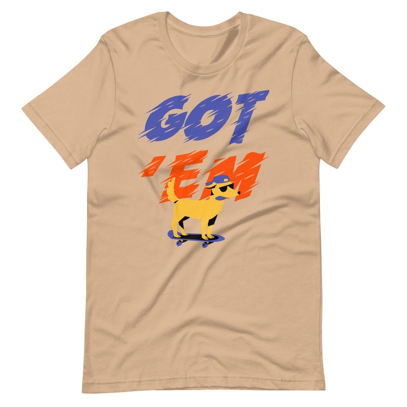 May include: A tan t-shirt with the words "GOT 'EM" in blue and red lettering. A cartoon yellow dog wearing a blue hat and sunglasses is skateboarding.
