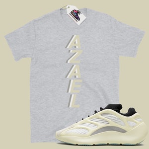 May include: A grey t-shirt with the word "AZAEL" printed vertically in a light beige color.  A pair of off-white sneakers with black accents.