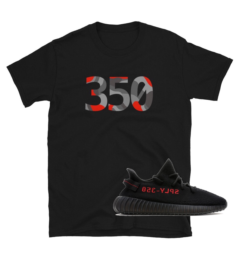 May include: Black t-shirt with a red and gray camouflage 350 graphic. A black and red Yeezy Boost 350 v2 sneaker is shown below the shirt.