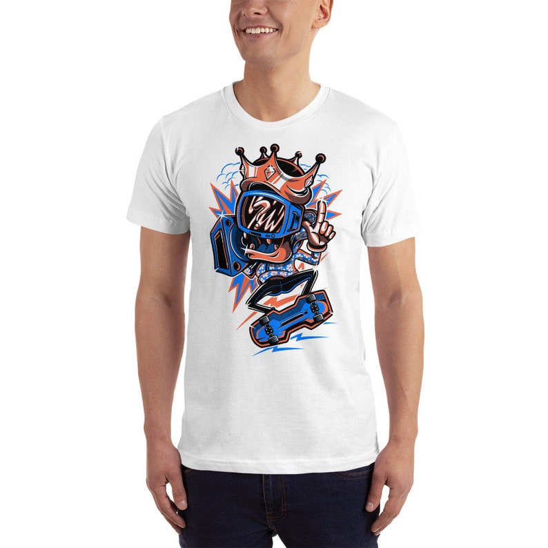 Pu&ograve; includere: Maglietta bianca con un'illustrazione di un cartone animato di una persona che indossa un casco blu e una corona, tiene un boombox e fa skateboard. La persona indossa una camicia a motivi blu e bianchi.