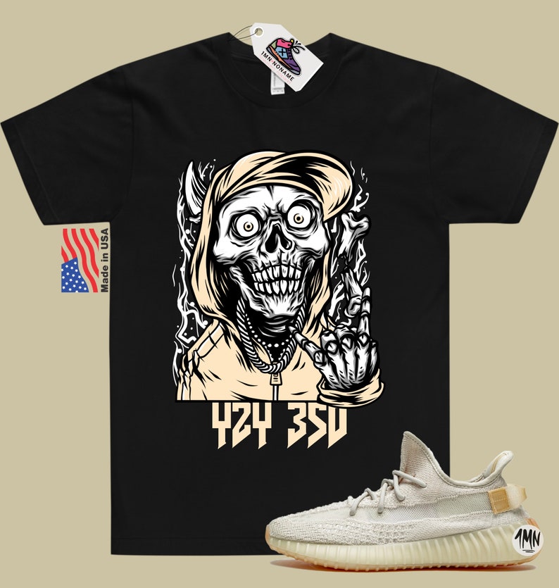 Puede incluir: Camiseta negra con un gr&aacute;fico de una calavera con capucha haciendo un gesto con la mano. El texto "424 350" est&aacute; impreso debajo del gr&aacute;fico. Un par de zapatillas blancas y beige con suela marr&oacute;n se muestran en la esquina inferior derecha de la imagen.