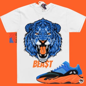 May include: White t-shirt with a blue lion graphic and the word "BEAST" printed below. The shirt is paired with blue and orange sneakers.