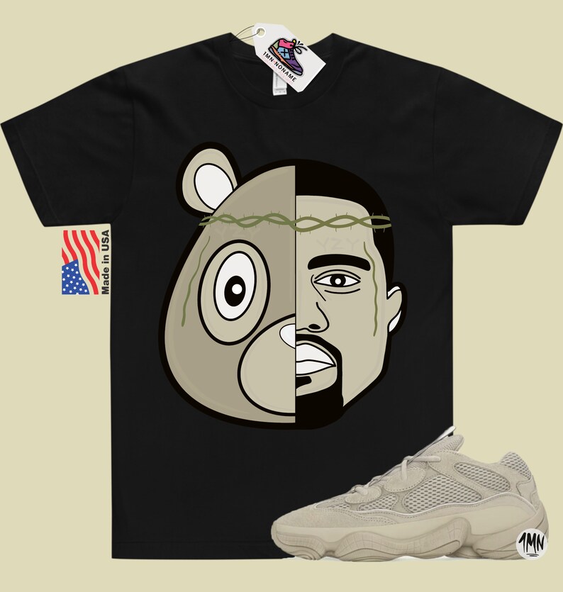 May include: Black t-shirt with a graphic of a bear and Kanye West's face. The graphic is split down the middle, with the bear on the left and Kanye on the right. The bear has a crown of thorns on its head.  A pair of beige Yeezy 500 sneakers are shown below the t-shirt.