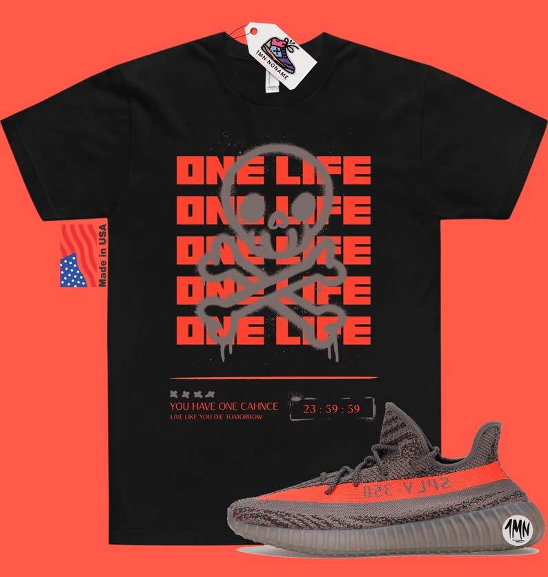 Puede incluir: Camiseta negra con un gr&aacute;fico de calavera y huesos cruzados grises y el texto "ONE LIFE" repetido cinco veces en rojo. La camiseta se combina con zapatillas grises y naranjas con el texto "Yeezy" en el lateral.