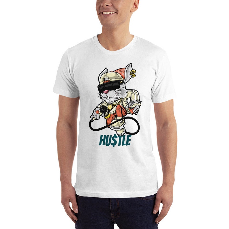 May include: White t-shirt featuring a cartoon rabbit wearing a hat, sunglasses, and holding a microphone. The rabbit is standing on an infinity symbol with the word "HU$TLE" beneath it.