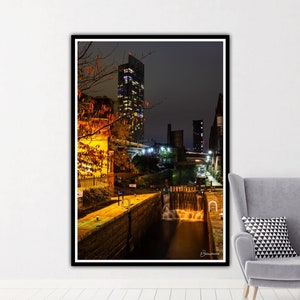 May include: A nighttime view of a city skyline with a tall building illuminated in the distance. A canal runs through the foreground, with a lock gate and water flowing through it. The scene is lit by streetlights and the glow of the city.