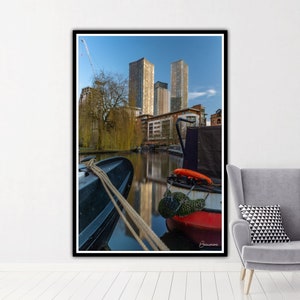 May include: A photograph of a canal in a city with tall buildings in the background. Two boats are docked in the canal, one is red and the other is black. The water is calm and reflects the buildings.