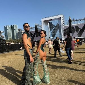 Puede incluir: Dos personas posan al aire libre con atuendos de festival. Una persona lleva un body verde con pantalones de perlas de pierna abierta. La otra persona lleva un arn&eacute;s verde y pantalones con estampado de leopardo. Ambos llevan gafas de sol.
