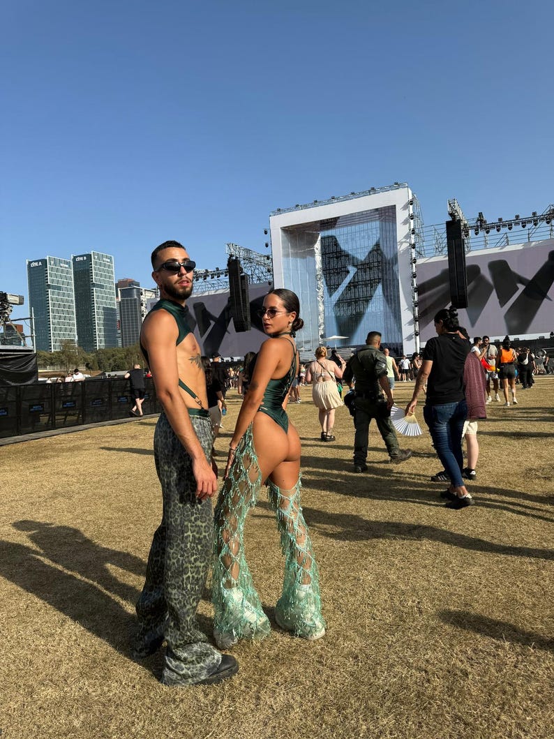 Puede incluir: Dos personas posan al aire libre con atuendos de festival. Una persona lleva un body verde con pantalones de perlas de pierna abierta. La otra persona lleva un arn&eacute;s verde y pantalones con estampado de leopardo. Ambos llevan gafas de sol.