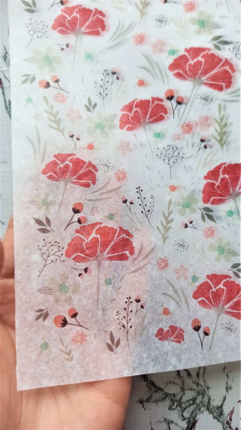 May include: White tissue paper with a floral pattern. The pattern features red flowers with green leaves and stems. There are also smaller pink and green flowers throughout the design.