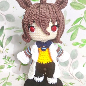May include: A handmade crochet doll with brown hair and red eyes, wearing a white lab coat over a yellow shirt and black pants. The doll has a detailed design and the text "Crochet Pattern" and "AGNES TACHYON" are visible.