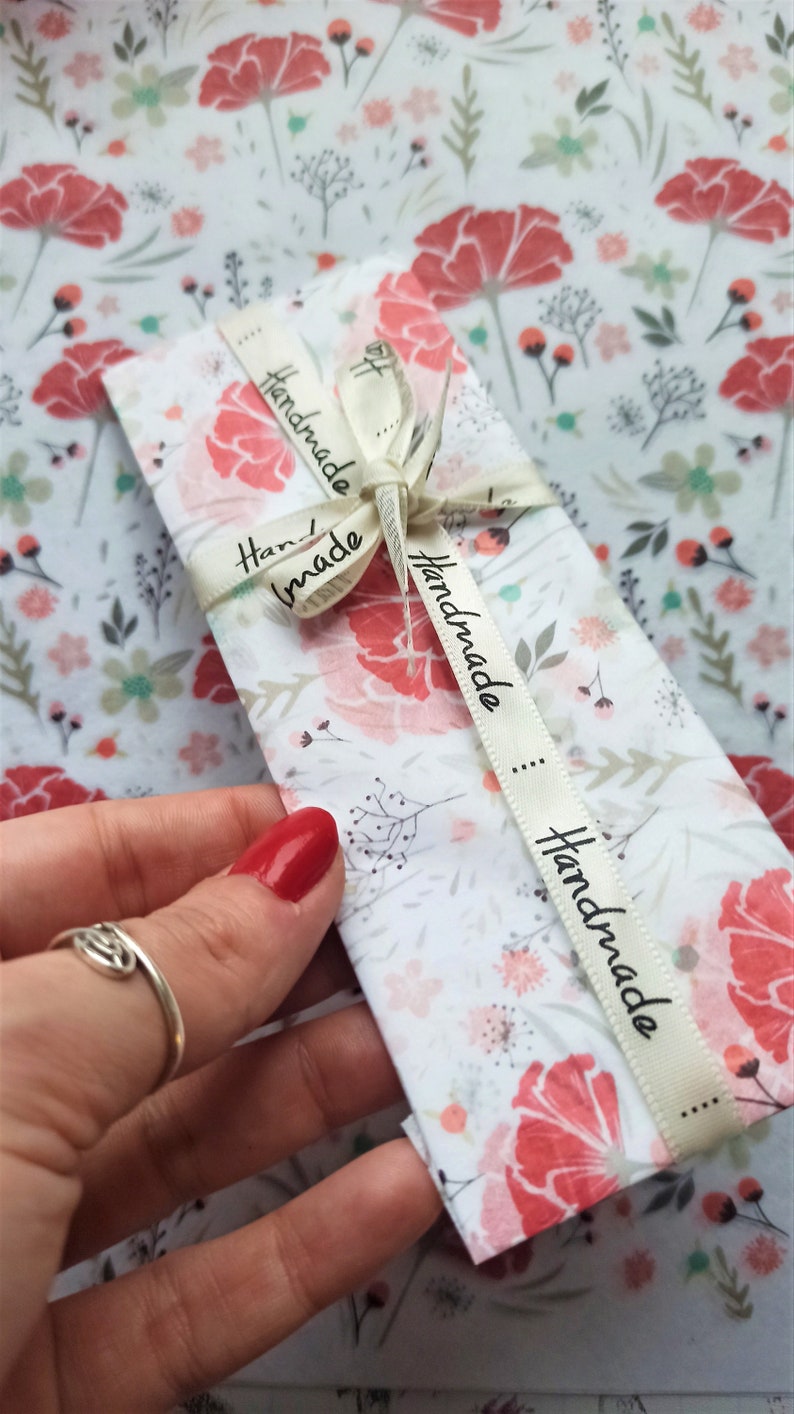 May include: A white envelope with a floral pattern and a cream ribbon tied around it. The ribbon has the word "Handmade" printed on it in black.