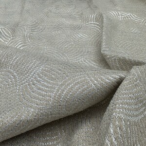 May include: Beige fabric with a silver metallic pattern of overlapping circles. The fabric has a textured, woven look.