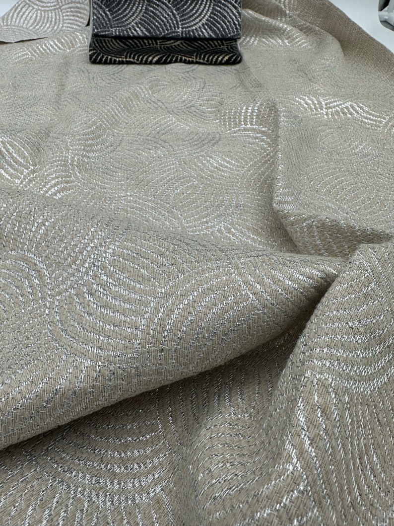 May include: Beige fabric with a silver metallic pattern of overlapping circles. The fabric has a textured, woven look.