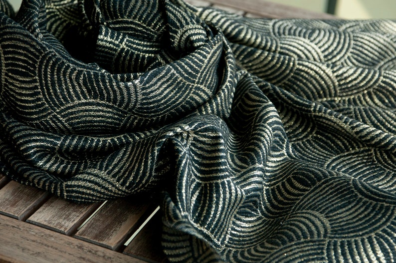 May include: A black and gold scarf with a geometric pattern of overlapping circles. The scarf is made of a soft, textured fabric.