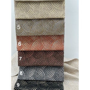 May include: A close-up of five fabric swatches with a geometric pattern. The swatches are arranged in a stack, with the top swatch being a light beige color, followed by a darker beige, a reddish-orange, a dark brown, and a black and white swatch. The swatches are numbered 5 through 9.
