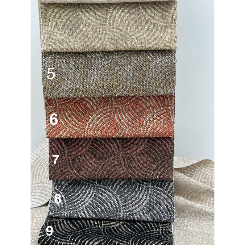 May include: A close-up of five fabric swatches with a geometric pattern. The swatches are arranged in a stack, with the top swatch being a light beige color, followed by a darker beige, a reddish-orange, a dark brown, and a black and white swatch. The swatches are numbered 5 through 9.