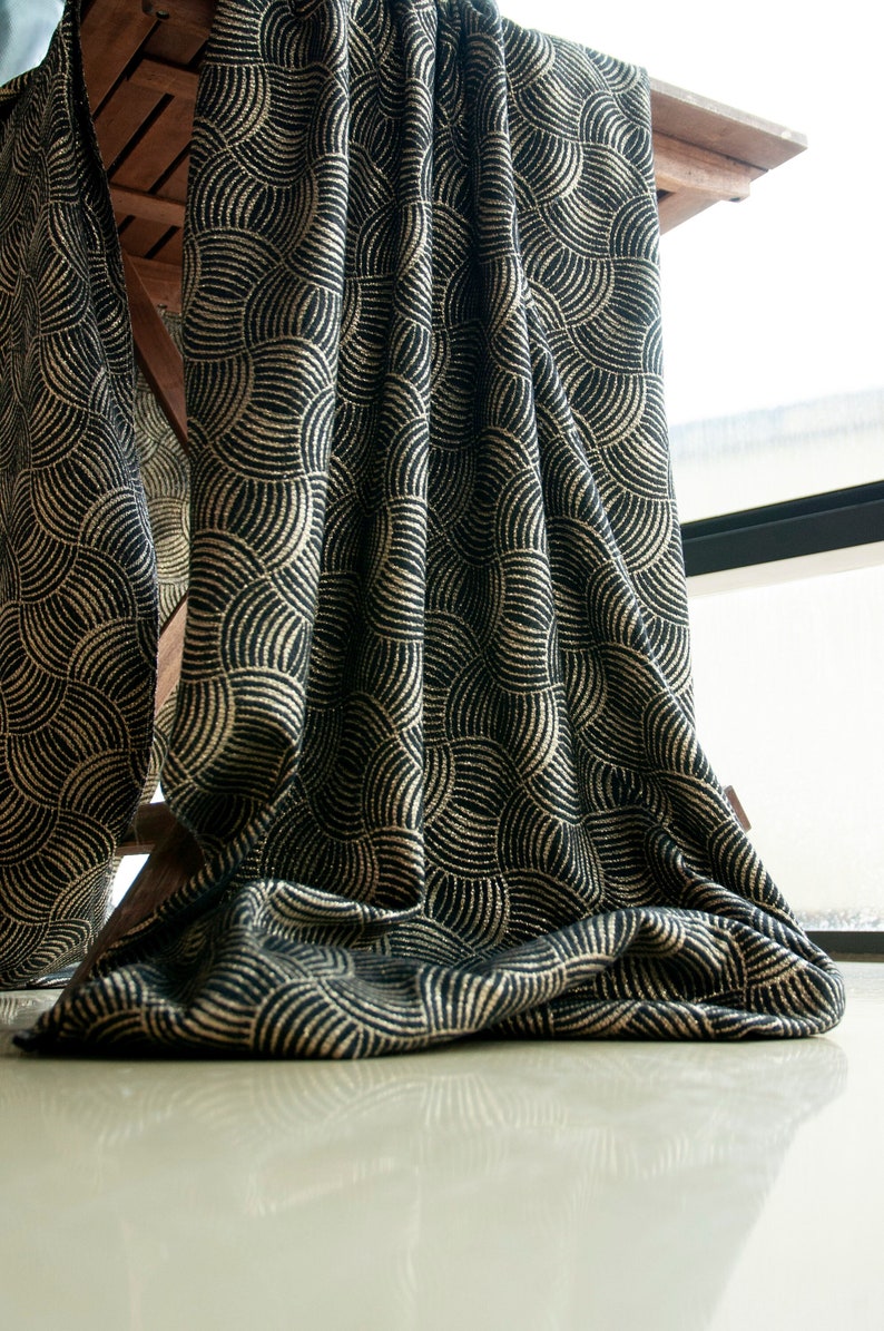 May include: Black fabric with a gold geometric pattern. The fabric is draped over a wooden table and hangs down to the floor.