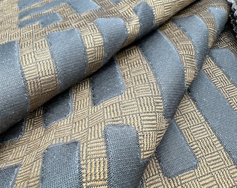 May include: Close-up of a fabric with a geometric pattern. The fabric is a dark blue color with gold accents. The pattern is a series of interlocking squares and rectangles.