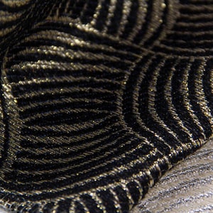May include: Close-up of a black and gold fabric with a geometric pattern. The fabric has a subtle sheen and a textured surface.