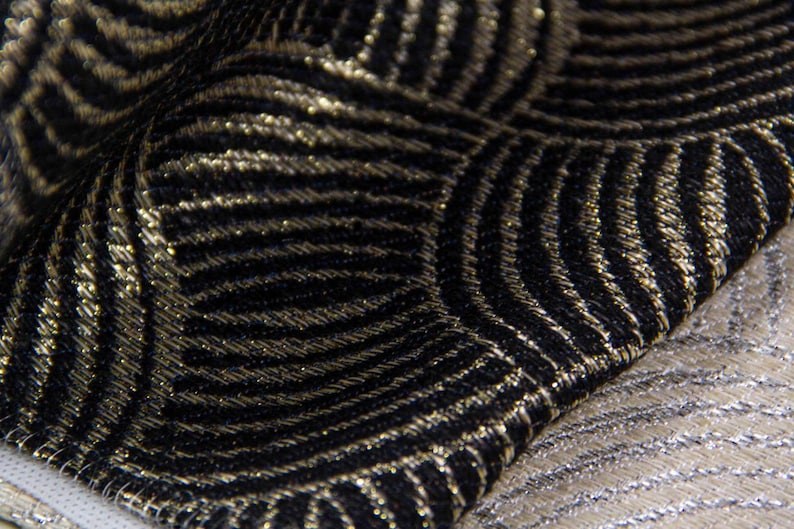 May include: Close-up of a black and gold fabric with a geometric pattern. The fabric has a subtle sheen and a textured surface.