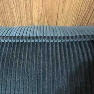 Slate blue ribbed velvet upholstery fabric folded over wood, narrow ribs running across the surface