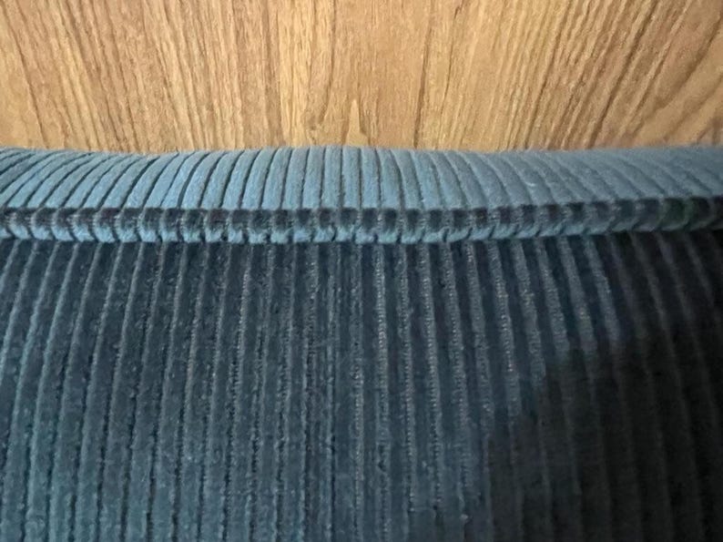 Slate blue ribbed velvet upholstery fabric folded over wood, narrow ribs running across the surface