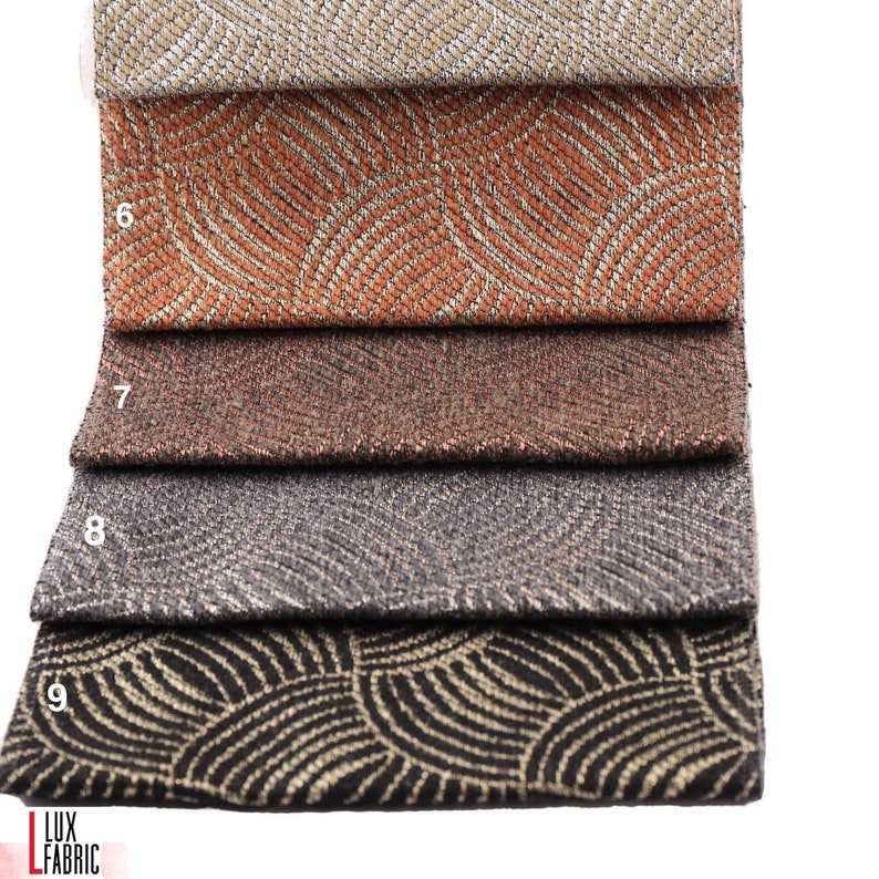 May include: Four fabric swatches with a geometric pattern in shades of beige, orange, brown, and black. The fabric has a subtle shimmer and a textured surface.