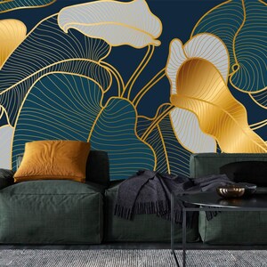 May include: A dark teal and gold leaf pattern wallpaper. The design features large leaves in gold, white, and teal, with gold outlines. A dark green sofa with an orange pillow is in front of the wallpaper.