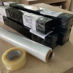 a collection of black and white boxes, some of which are wrapped in plastic, and a roll of clear tape on a table.