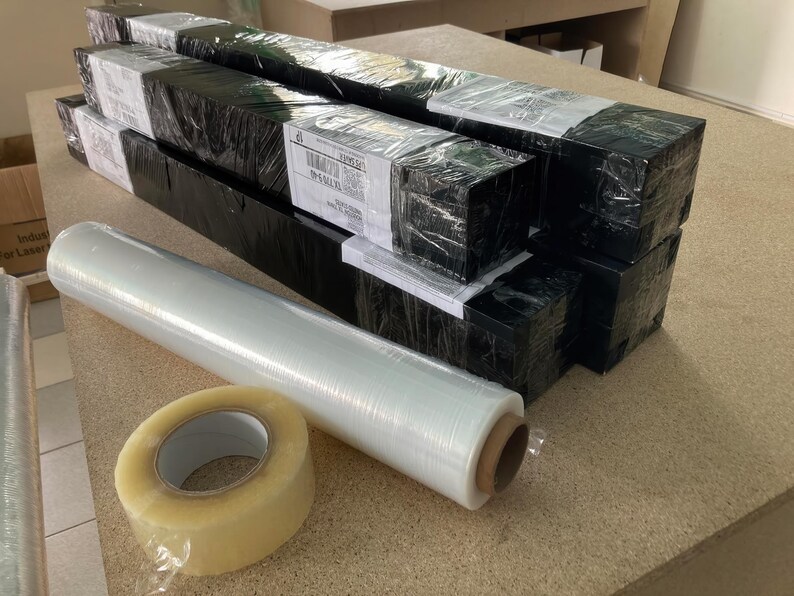 a collection of black and white boxes, some of which are wrapped in plastic, and a roll of clear tape on a table.
