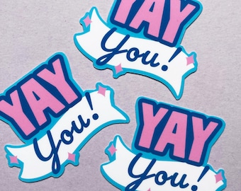 Puede incluir: Tres pegatinas rosas y azules con el texto "YAY You!" en una pancarta blanca con estrellas azules.