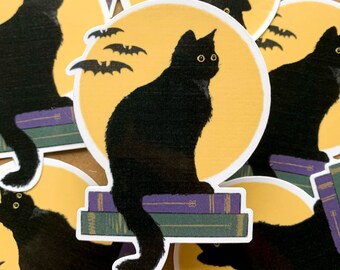 Puede incluir: Un gato negro sentado en una pila de libros frente a una luna amarilla con murciélagos volando a su alrededor.