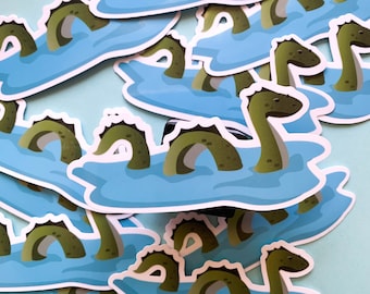 Puede incluir: Un conjunto de pegatinas coloridas que representan un monstruo marino de dibujos animados con un cuello largo y un cuerpo verde. Las pegatinas están sobre un fondo azul y tienen un contorno blanco.