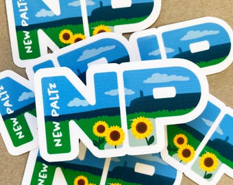 Puede incluir: Una pila de pegatinas con las letras "NP" en blanco con un cielo azul, hierba verde y girasoles amarillos. El texto "NEW PALTZ" está escrito verticalmente en el lado izquierdo de la pegatina.