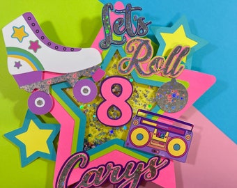 May include: A pink and blue birthday cake topper with a roller skate, a boombox, a star, and the text "Let's Roll" and "Cary's 8".