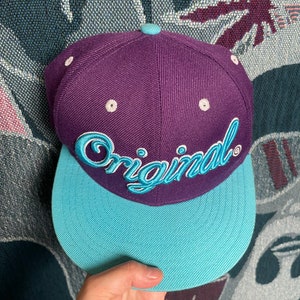 May include: A purple and blue baseball cap with the word "Original" embroidered in blue on the front.