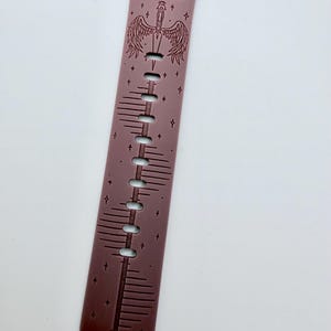 May include: A mauve silicone watch band featuring a dark engraved design of a sword with wings, small stars, and the text "VALKYRIE" and "NOTHING CAN BREAK ME" printed in a dark font. The band includes multiple adjustment holes along the center.