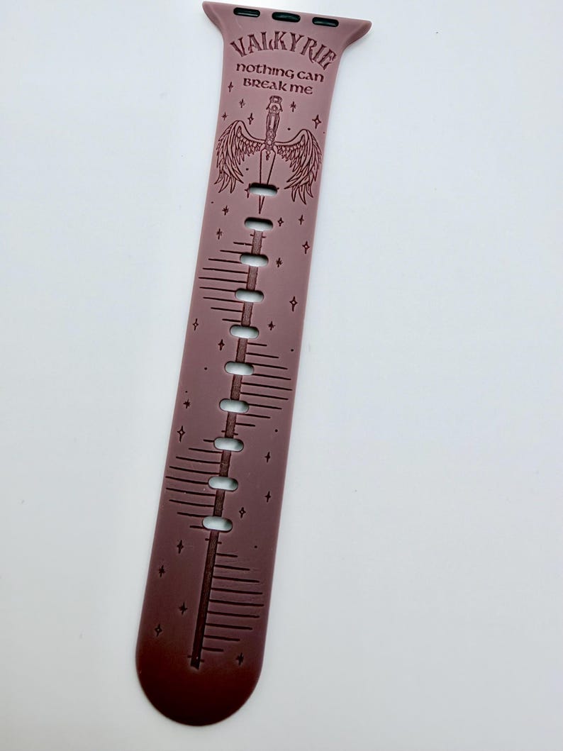 May include: A mauve silicone watch band featuring a dark engraved design of a sword with wings, small stars, and the text "VALKYRIE" and "NOTHING CAN BREAK ME" printed in a dark font. The band includes multiple adjustment holes along the center.